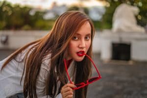 girl with red lips and red hair biting on red sunglasses