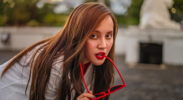 girl with red lips and red hair biting on red sunglasses