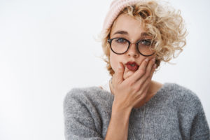 blond girl with red lipstick pink hat and curly hair making a face